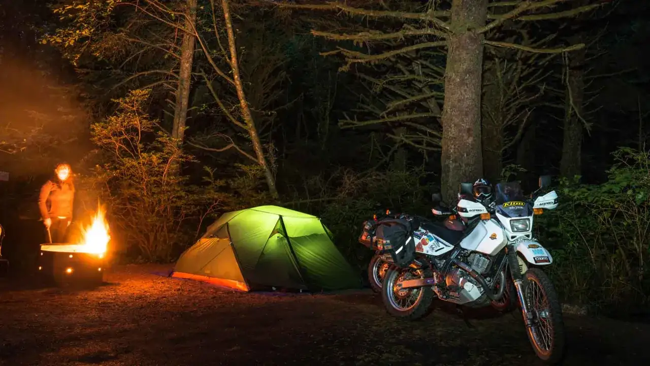 Nocne biwakowanie w lesie: zielony namiot, motocykl i ognisko. Idealny zestaw, jaki namiot na motocykl sprawdzi się w takich warunkach.