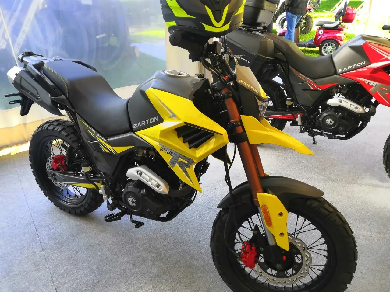 Żółty motocykl Barton Hyper 125, gotowy na zwiększenie mocy. Widoczny kask i inne motocykle w tle.