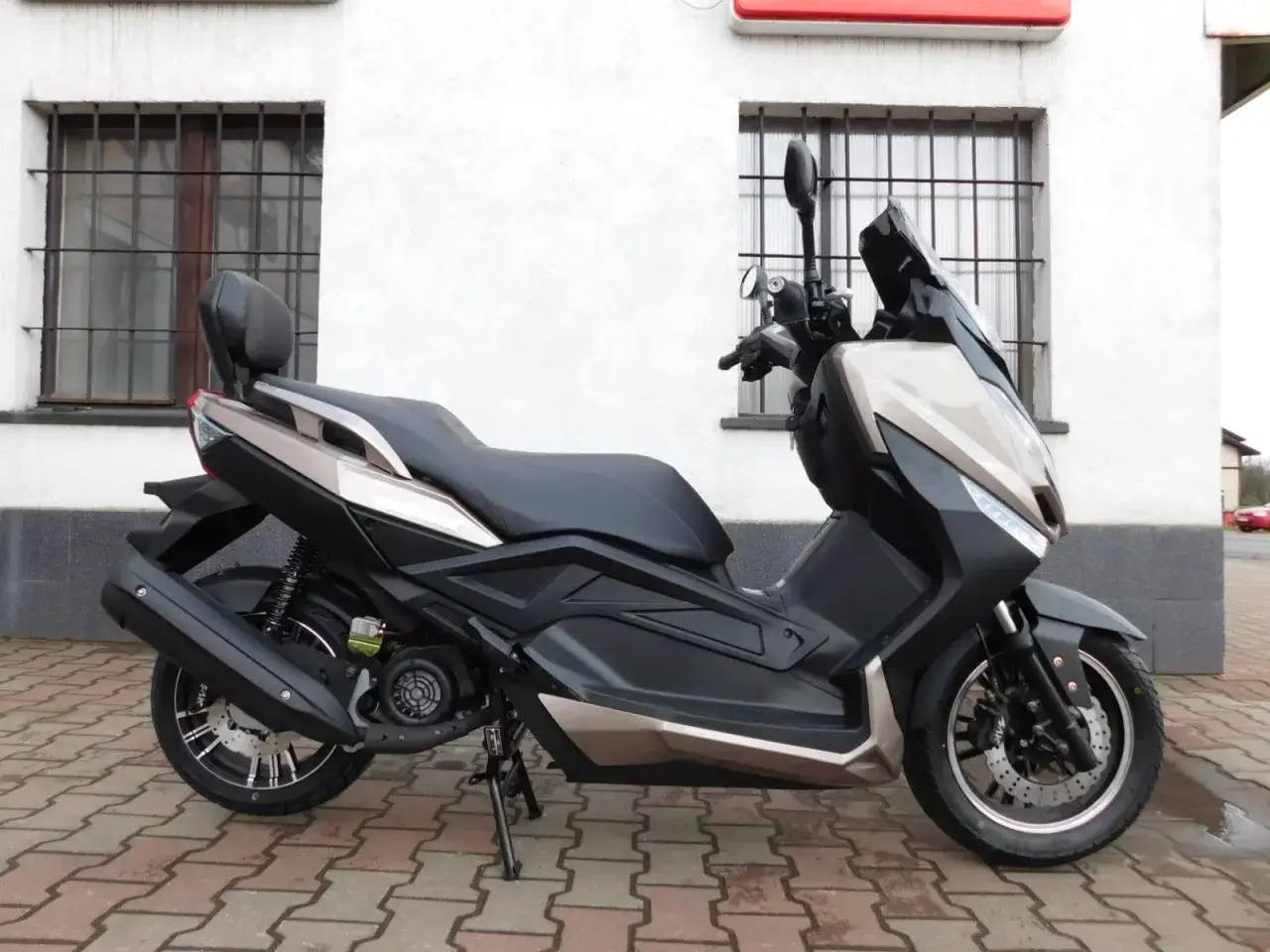 Elegancki skuter Zipp QR Max 125 w kolorze czarno-beżowym, zaparkowany przed budynkiem z kratami w oknach.