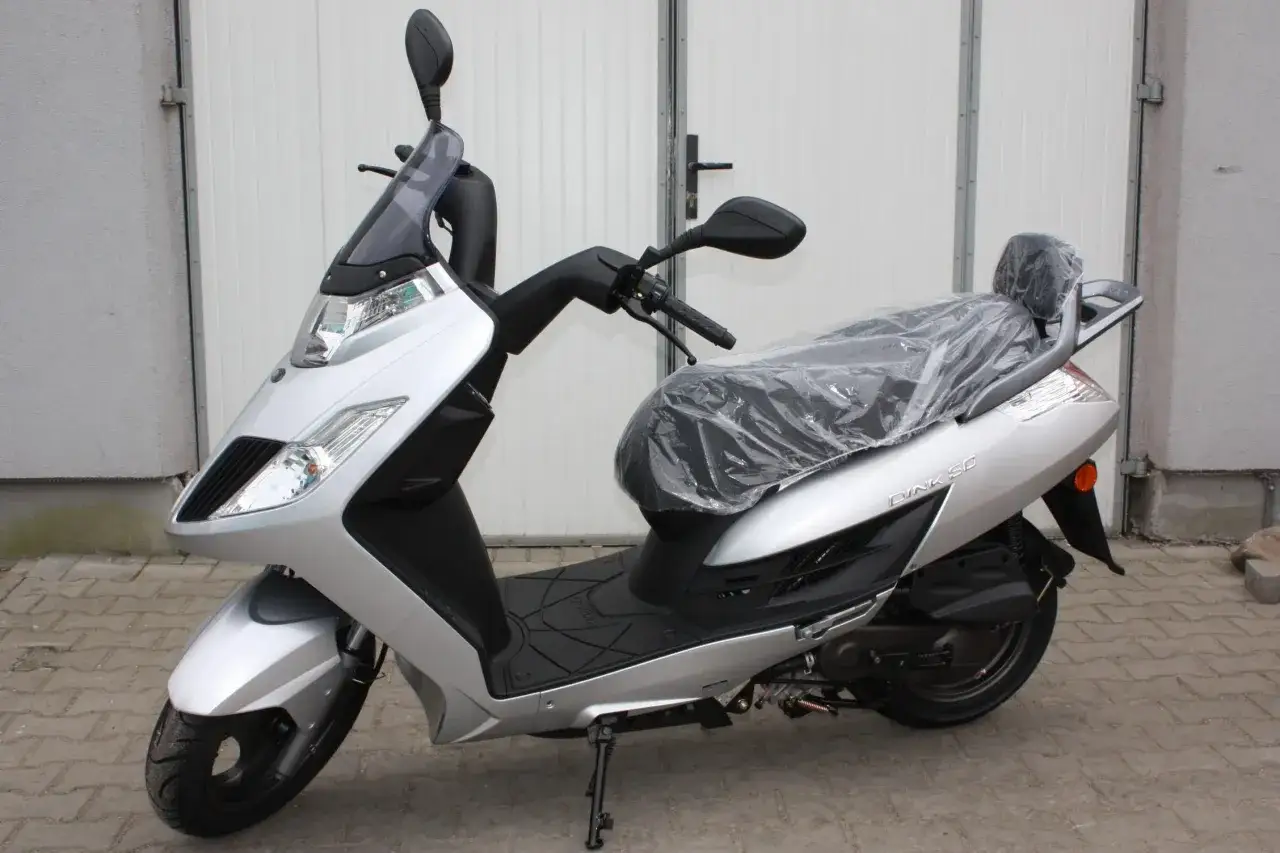 Srebrny skuter Kymco Dink 50 z przykrytym siedzeniem, gotowy do jazdy po miejskich ulicach.