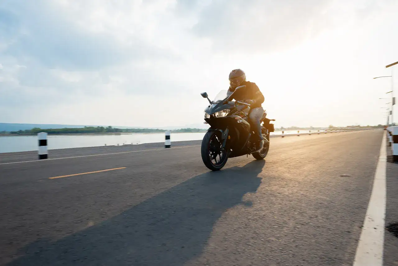 Motocyklista przemierza malownicze trasy motocyklowe zachodniopomorskie. Słońce odbija się od wody, tworząc magiczną atmosferę.