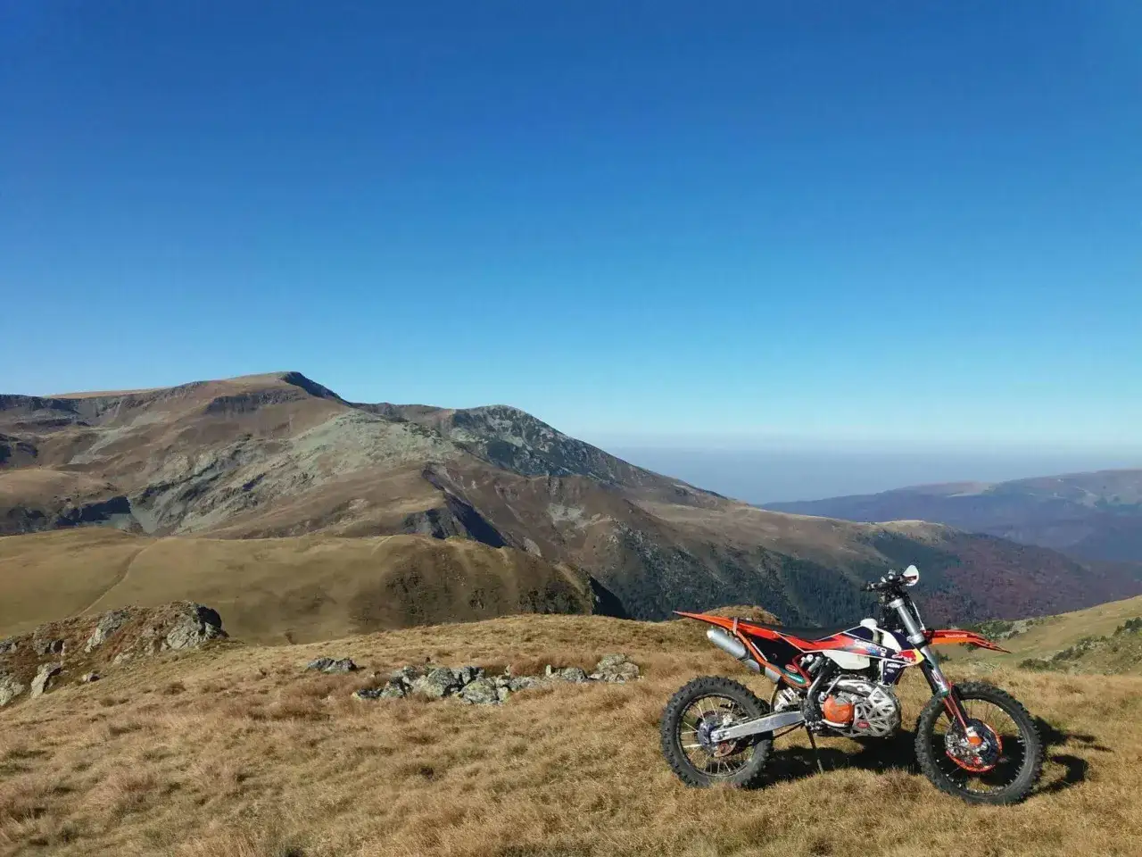 Pomarańczowy motocykl terenowy na tle g&oacute;rskiej panoramy. Idealne miejsce na trasę motocyklową w Rumunii.