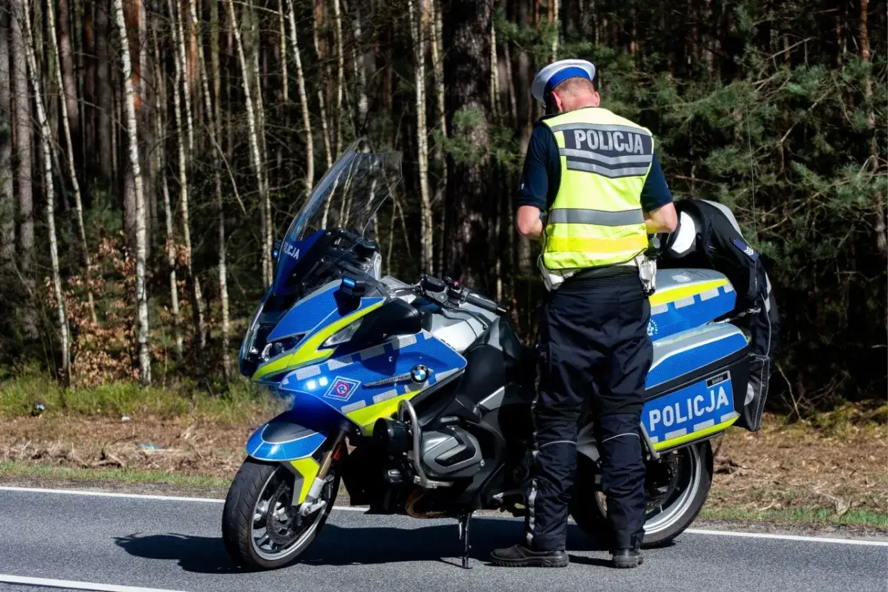 Policjant przy motocyklu wypisuje mandat za brak kategorii A. Las w tle.