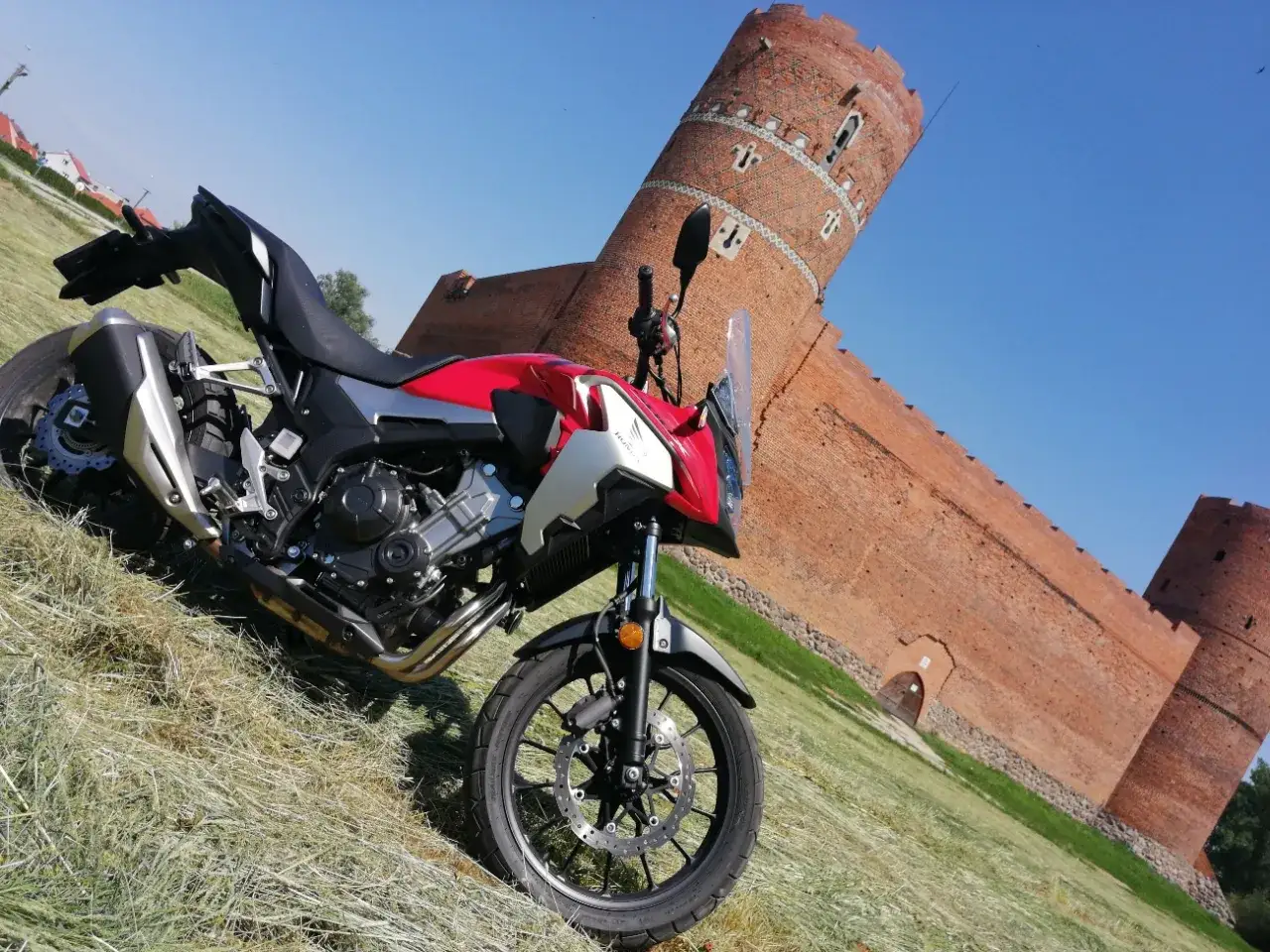 Czerwony motocykl na tle ceglanej twierdzy. Idealne miejsce na odkrywanie mazowieckich tras motocyklowych.