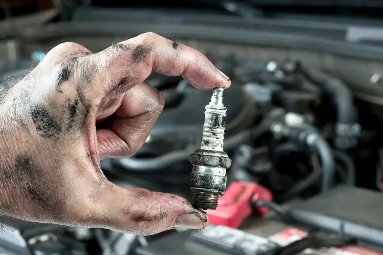 Brudna ręka mechanika trzyma zużytą świecę zapłonową. To jeden z objaw&oacute;w problem&oacute;w z silnikiem.