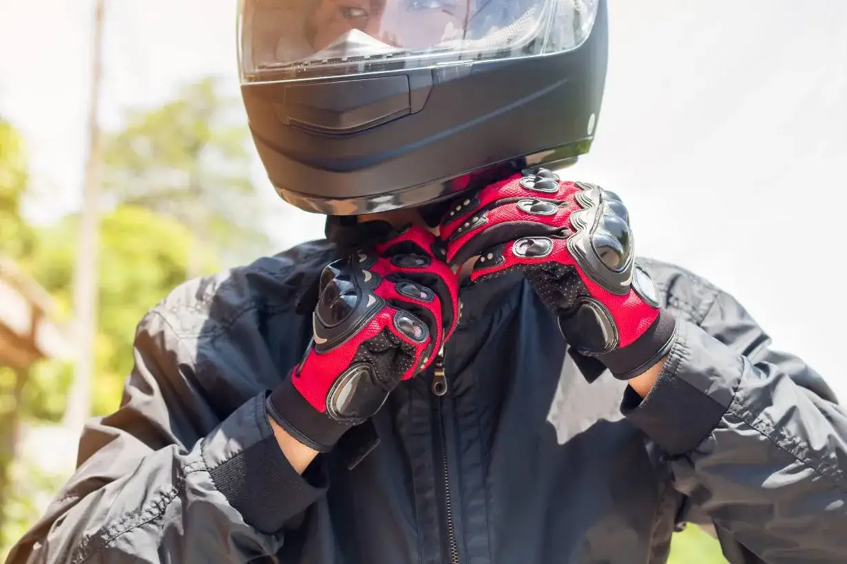 Motocyklista zapina rękawice, gotowy do jazdy w kasku. R&oacute;żne marki kask&oacute;w motocyklowych oferują bezpieczeństwo i styl.