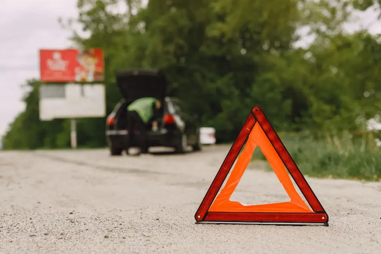 Trójkąt ostrzegawczy na drodze, z tyłu auto z otwartym bagażnikiem. Czy można holować na drodze ekspresowej?