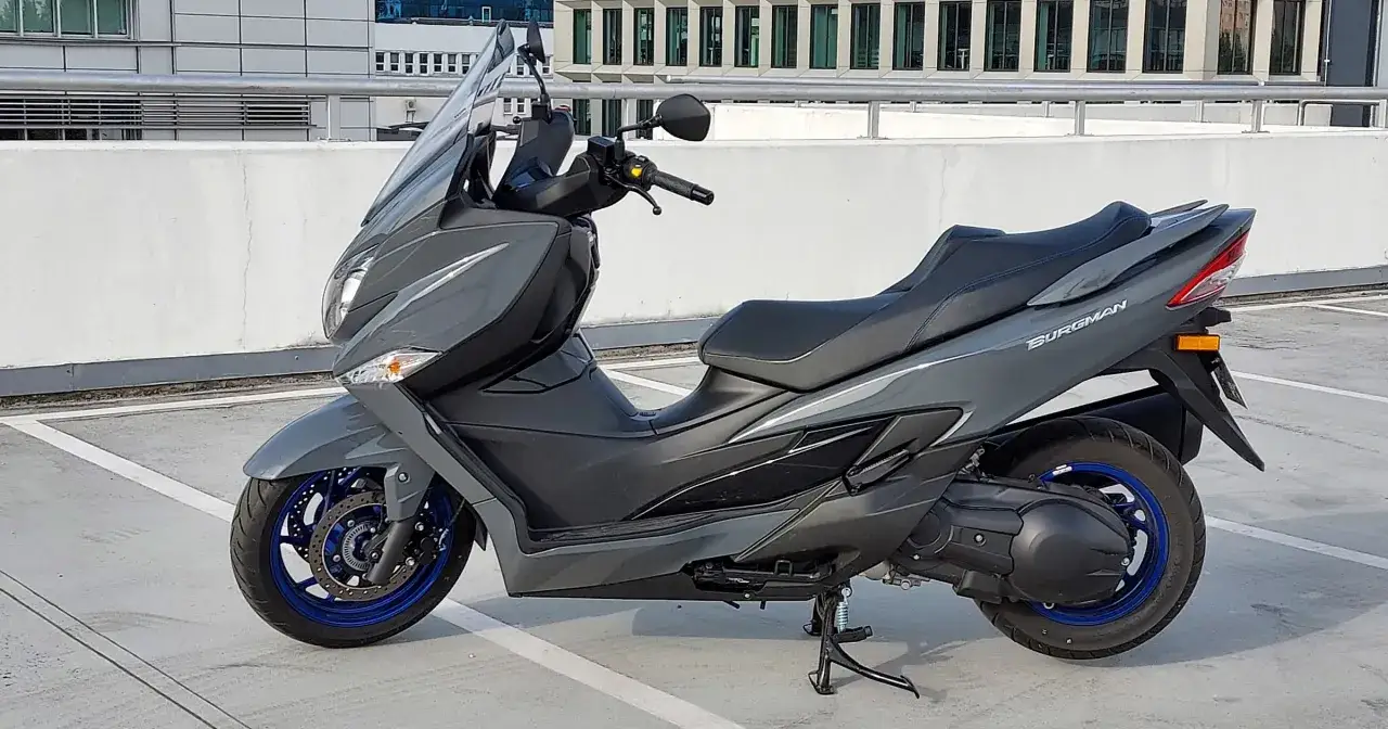 Szary Suzuki Burgman 400 na parkingu. Zastanawiasz się nad jego wadami i zaletami? Ten skuter to komfort i styl.