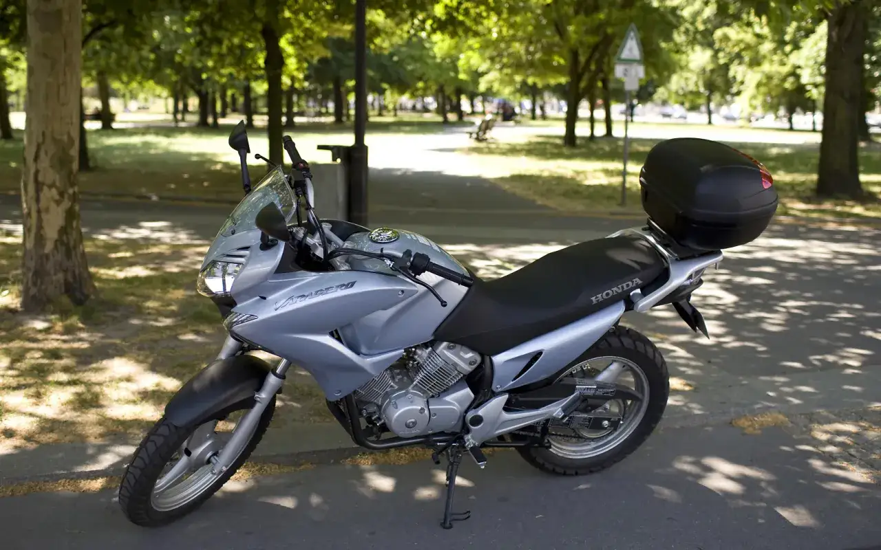 Srebrny motocykl Honda Varadero 125, gotowy do odblokowania mocy, zaparkowany w cieniu drzew.
