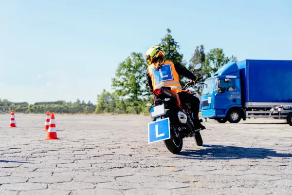 Osoba na motocyklu z literą "L" na kamizelce i tablicy, ćwiczy jazdę. Mam prawo jazdy B, chcę zrobić A.