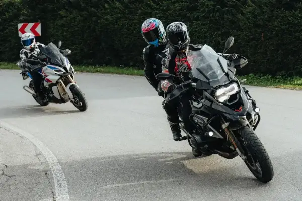 Motocykliści na zakręcie, jeden z pasażerem. Płynna zmiana biegów bez sprzęgła to klucz do dynamicznej jazdy.