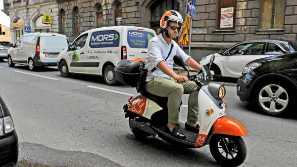 Mężczyzna w kasku jedzie skuterem elektrycznym, przygotowując się do testu na kartę motorowerową.