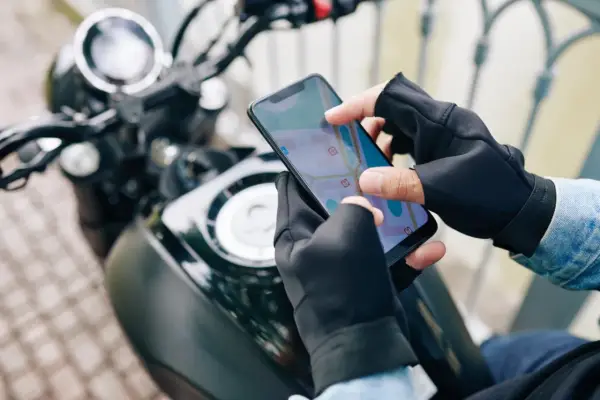 Motocyklista w rękawiczkach sprawdza trasę na mapie w aplikacji dla motocyklistów.