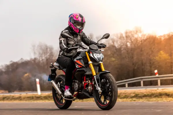 Motocyklistka w kolorowym kasku pędzi na czarnym motocyklu. Zastanawiasz się, ile waży litr benzyny, gdy tankujesz przed podróżą?