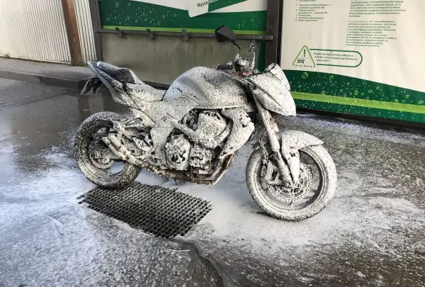 Motocykl pokryty pianą na myjni, gotowy do mycia. Instrukcja "jak myć motocykl" w tle.