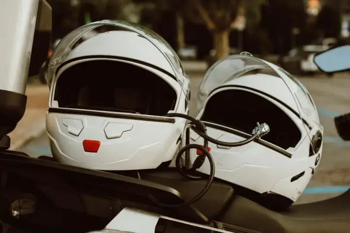Dwa białe kaski motocyklowe połączone blokadą. Gotowe do podróży, czekają na właścicieli.