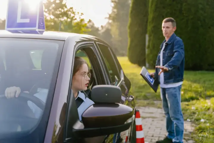 Młoda kursantka za kierownicą, instruktor objaśnia zasady. Zastanawia się, ile jest ważny egzamin teoretyczny na prawo jazdy.