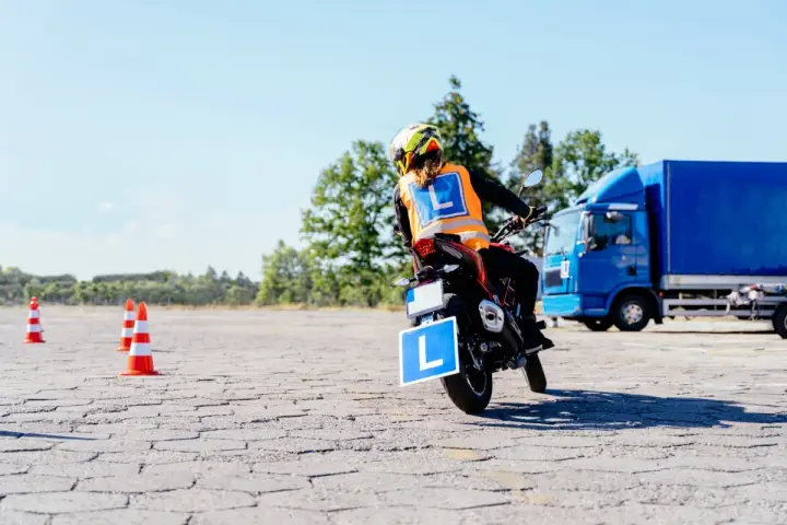Osoba na motocyklu z literą "L" na kamizelce i tablicy, ćwiczy jazdę. Mam prawo jazdy B, chcę zrobić A.