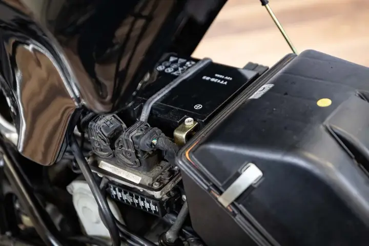 Akumulator motocyklowy w czarnej obudowie, gotowy do wymiany. Widać przewody i bezpieczniki. Prawidłowa wymiana akumulatora kolejność jest kluczowa.
