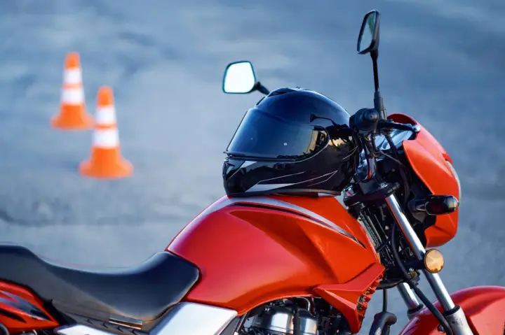 Pomarańczowy motocykl z kaskiem na baku i pachołkami w tle. Czy na motor trzeba mieć prawo jazdy? Tak, do prowadzenia motocykla wymagane jest odpowiednie prawo jazdy.