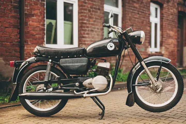 Czarny motocykl wsk 125 na tle ceglanego budynku. Klasyk z PRL-u gotowy do jazdy.