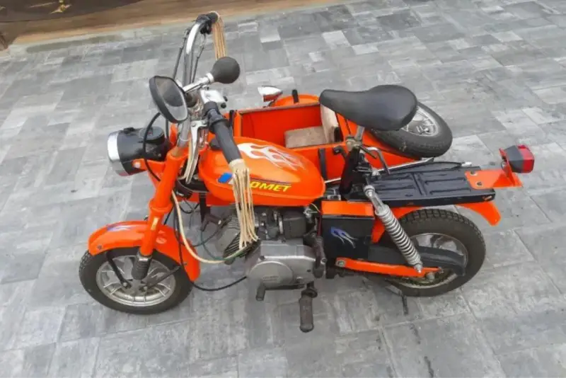 Pomarańczowa motorynka z koszem, ozdobiona płomieniami, gotowa na przejażdżkę.